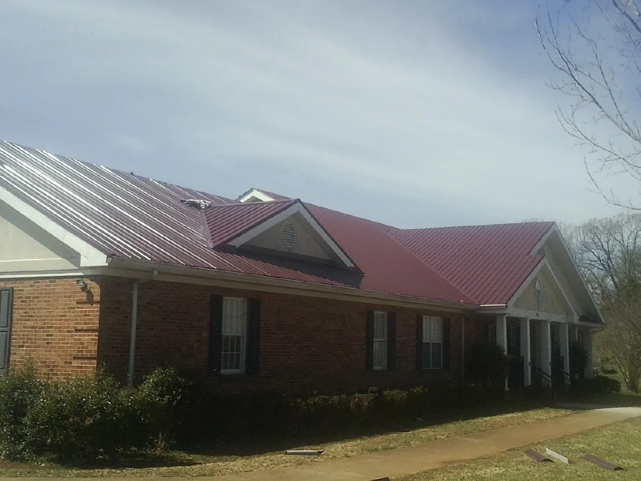 Red metal roof with gabled entries on a long brick building, from a Hail Damage Roof Repair job in Drewsey