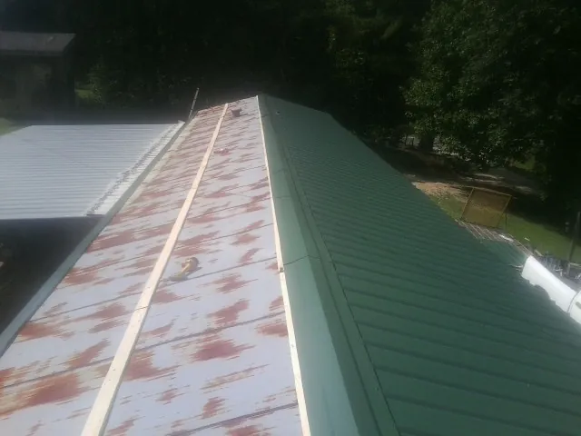 Old rusted panels beside newly installed green metal roofing — Wind Damage Roof Repair by Roofing Brothers in Drewsey