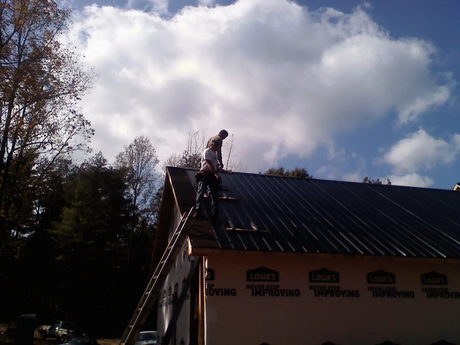 Roofer fastening dark metal panels high against a cloudy sky, from a Roof Inspection job in Drewsey