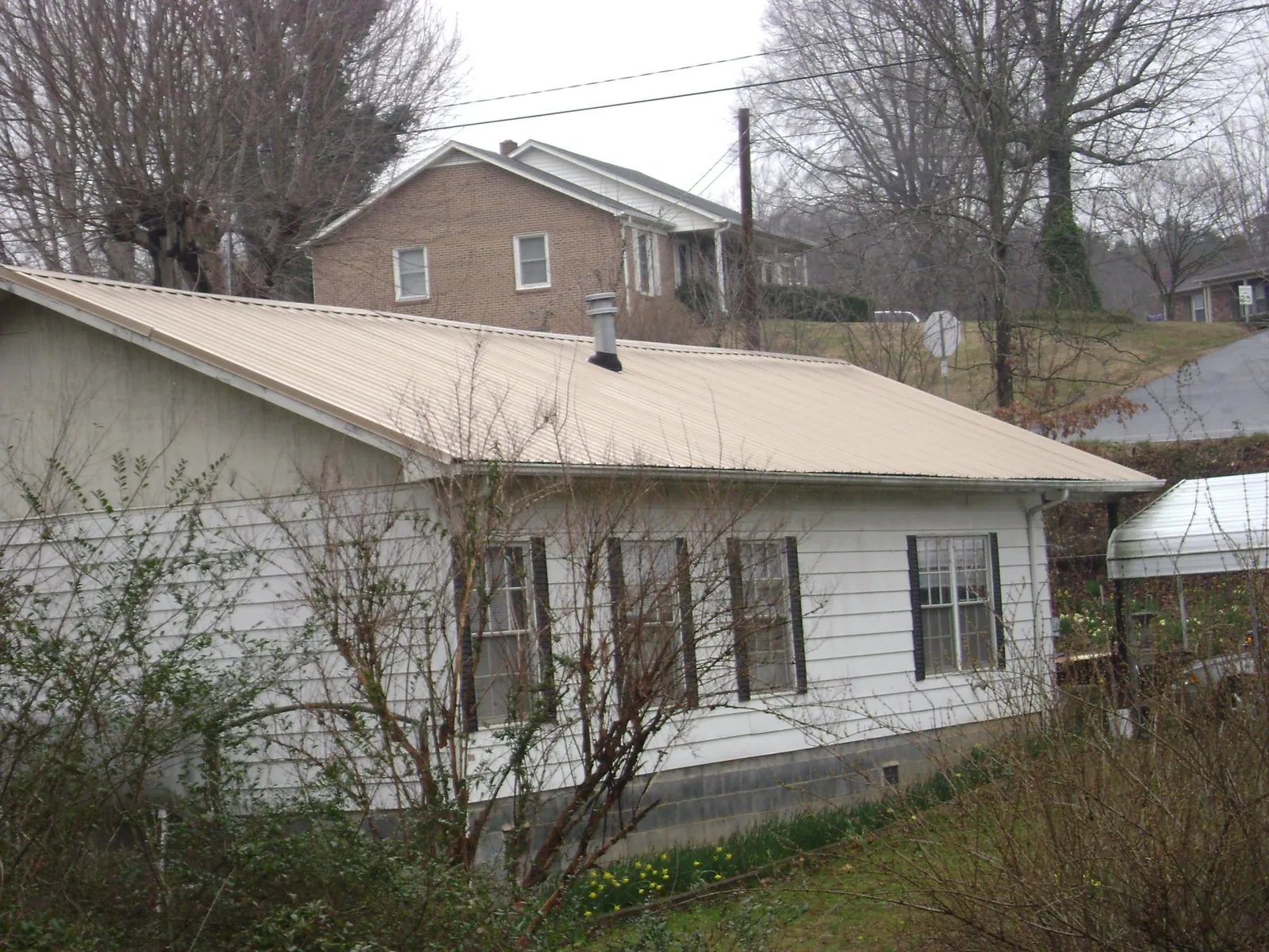 Tan metal roof on a white sided house set into a hillside — Commercial Roofing by Roofing Brothers in Drewsey
